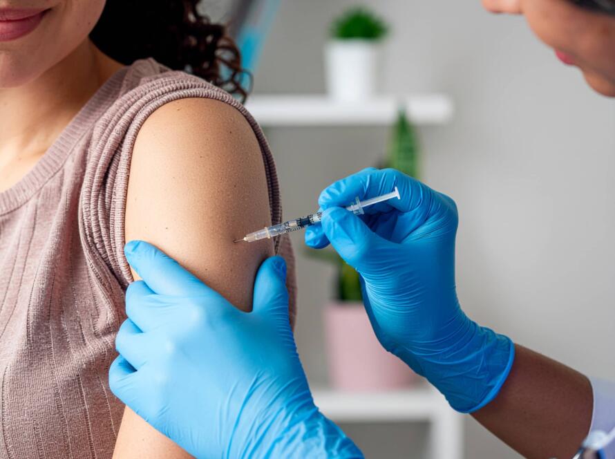 Κορίτσι λαμβάνει εμβόλιο στο χέρι από ιατρικό προσωπικό με γάντια, σε εσωτερικό χώρο.