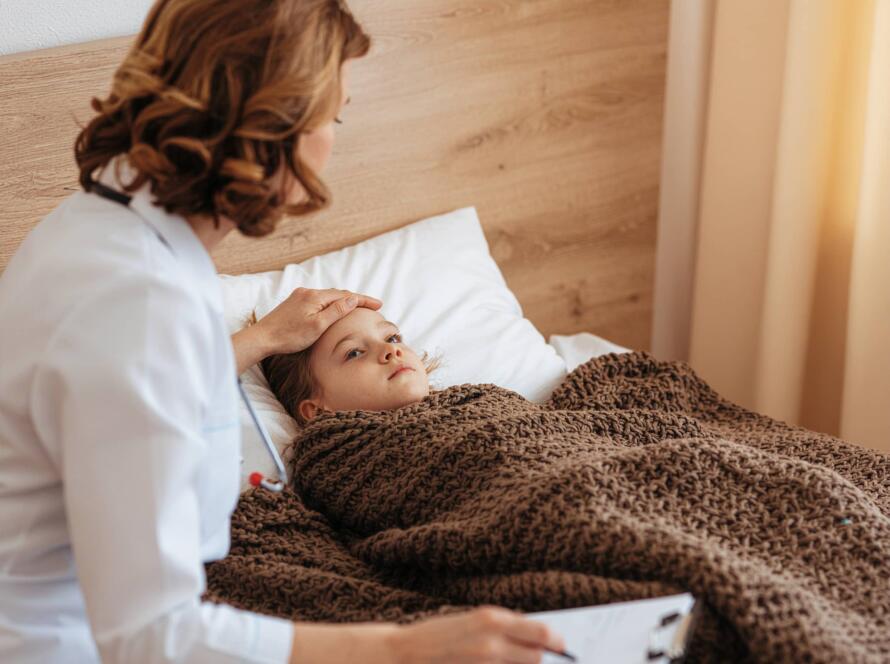Services 1 Γιατρός εξετάζει άρρωστο παιδί στο κρεβάτι, ελέγχοντας το μέτωπο για πυρετό σε κατ'οίκον επίσκεψη.