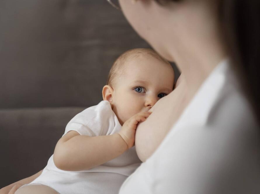 Services 3 Μητέρα θηλάζει το μωρό της φορώντας λευκή ρόμπα, προβάλλοντας τη στοργή και τη σημασία του μητρικού θηλασμού.